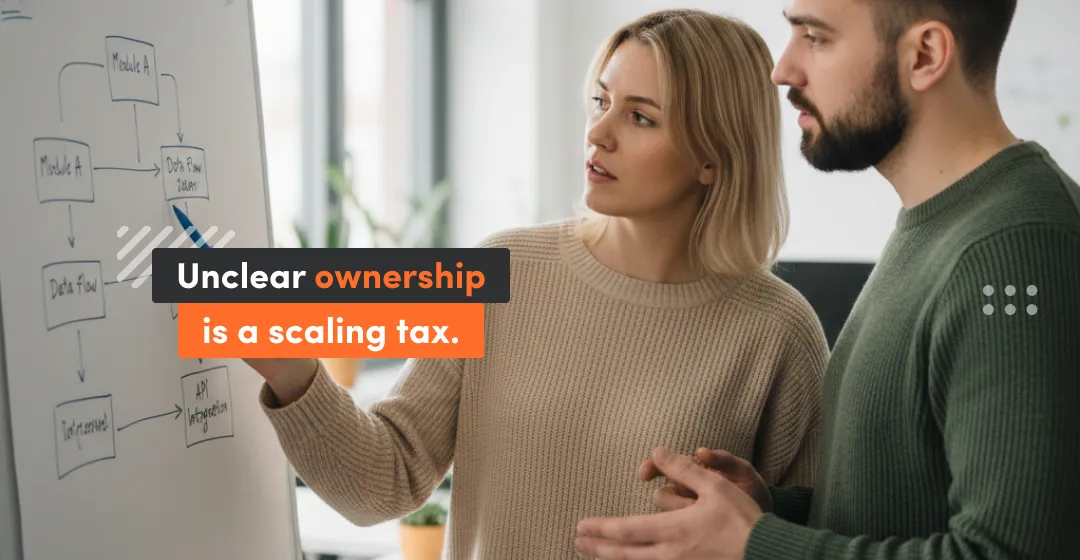 Two engineering leaders discussing a technical flowchart on a whiteboard, representing the need to define ownership and eliminate the scaling tax before hiring.