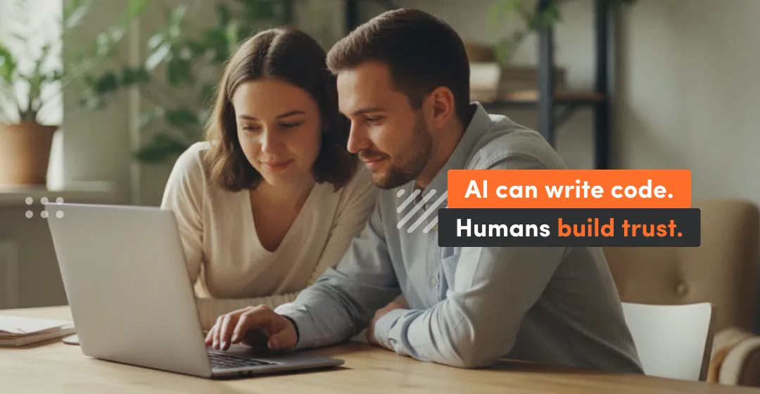 two people at the desk with dekstop and incsciption that AI can write code but humans build trust
