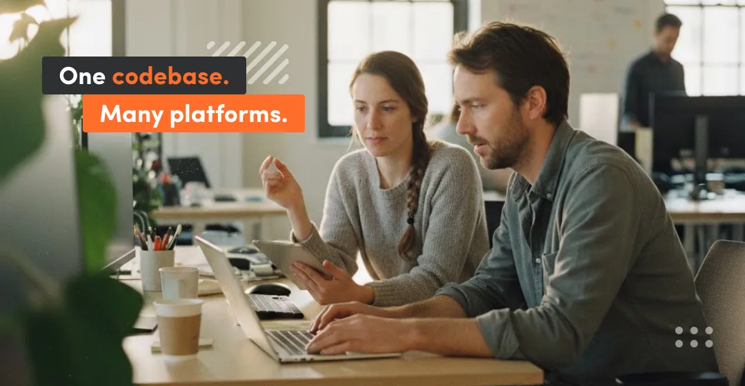 Two developers working together on a laptop and tablet while discussing a single codebase approach for hybrid or cross-platform apps.